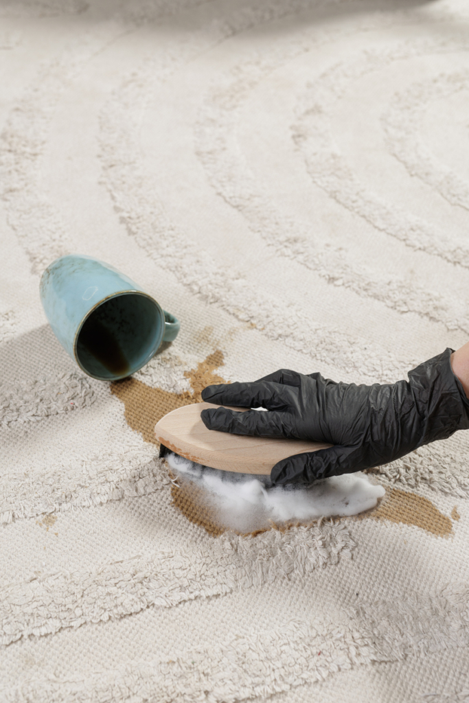 Gumikesztyűs kéz kefével súrolja a kávéfoltot a szőnyegből