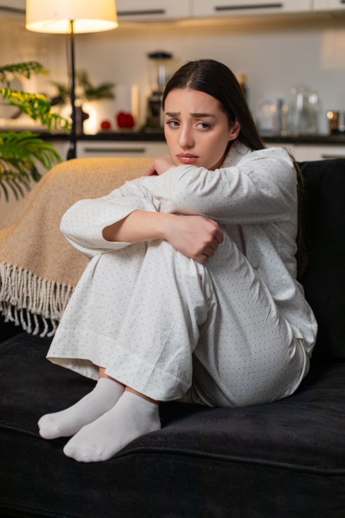 Szomorú nő felhúzott térdekkel ül az ágyon