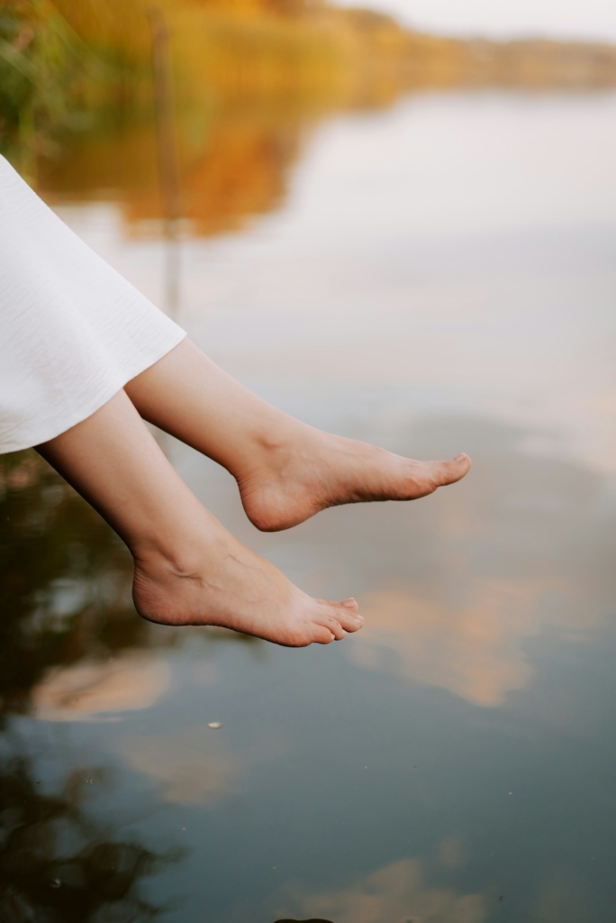 Nő lógatja a lábát egy tó mellett
