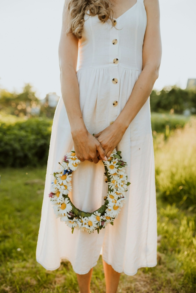 Nő egy virágos koszorúval a kezében egy napos réten