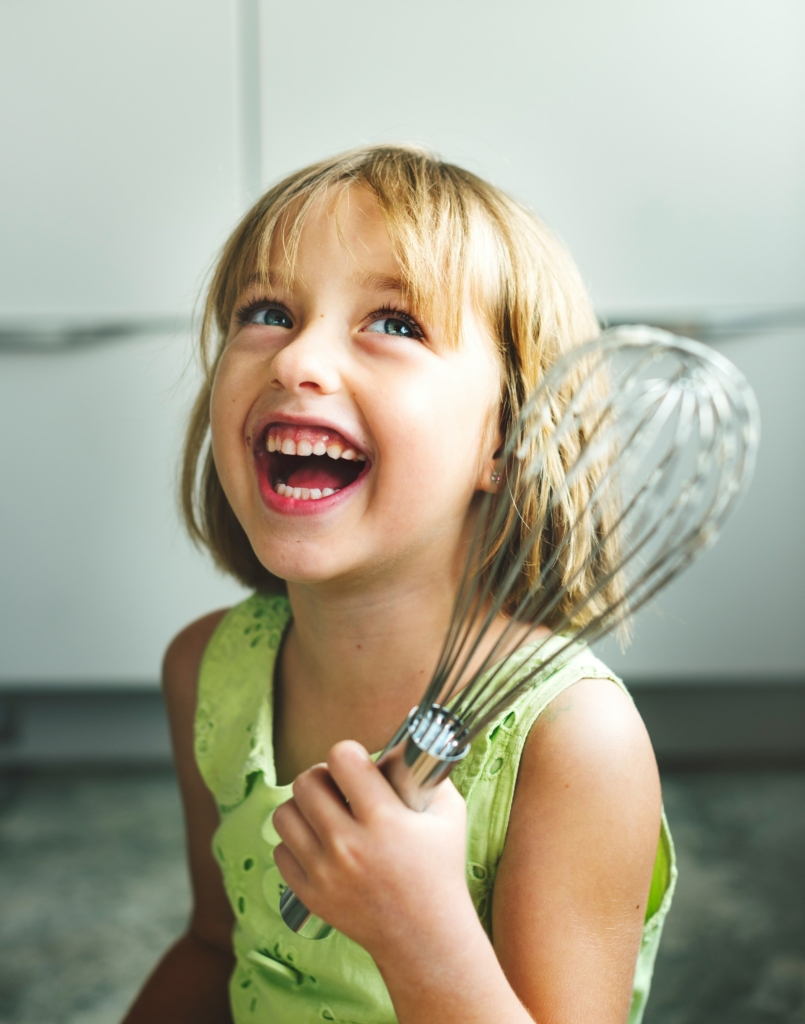 Mosolygós kislány egy habverővel a kezében