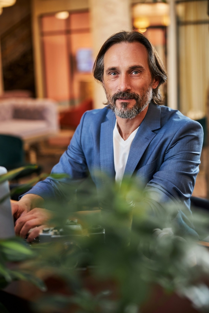 Középkorú, öltönyös férfi egy hotel halljában ül