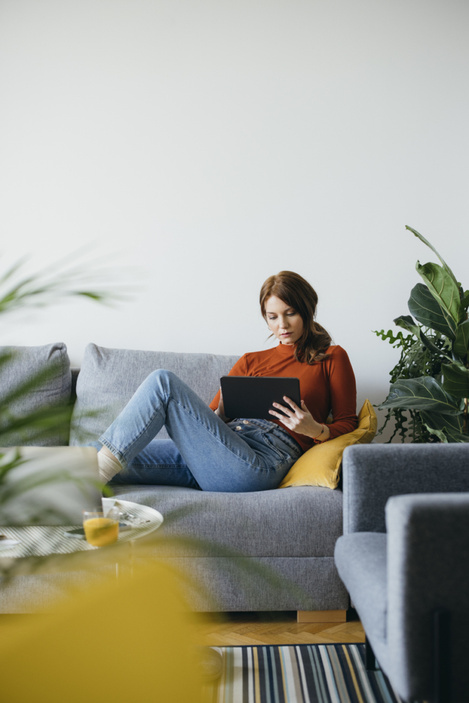 Nő a kanapén relaxál, közben tabletezik
