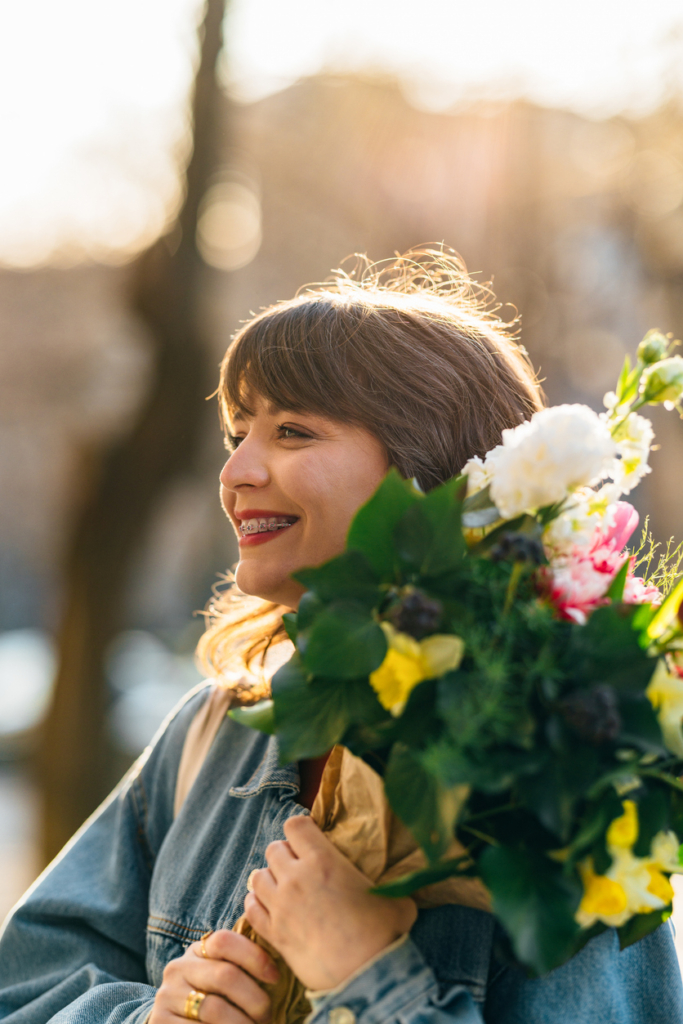 Mosolygós, fogszabályozós nő egy csokor virággal a szabadban