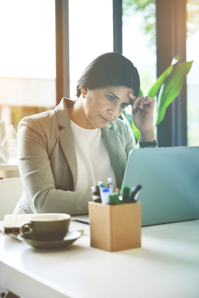 Középkorú nő stresszesen, fáradtan ül az irodában és dolgozik a laptopján