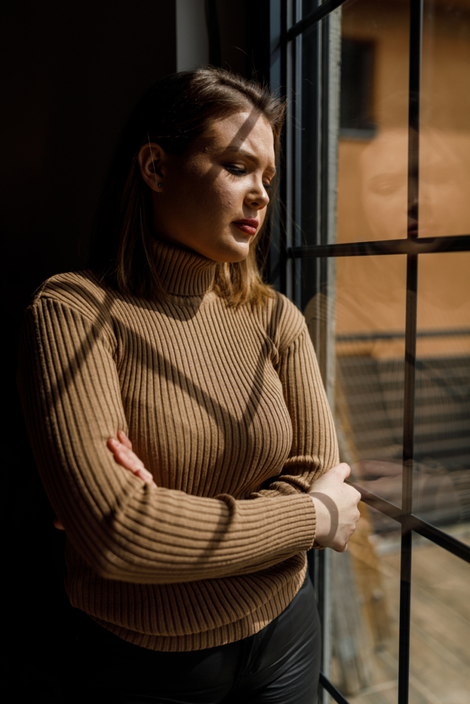 Szorongó, szomorú nő áll az ablaknál