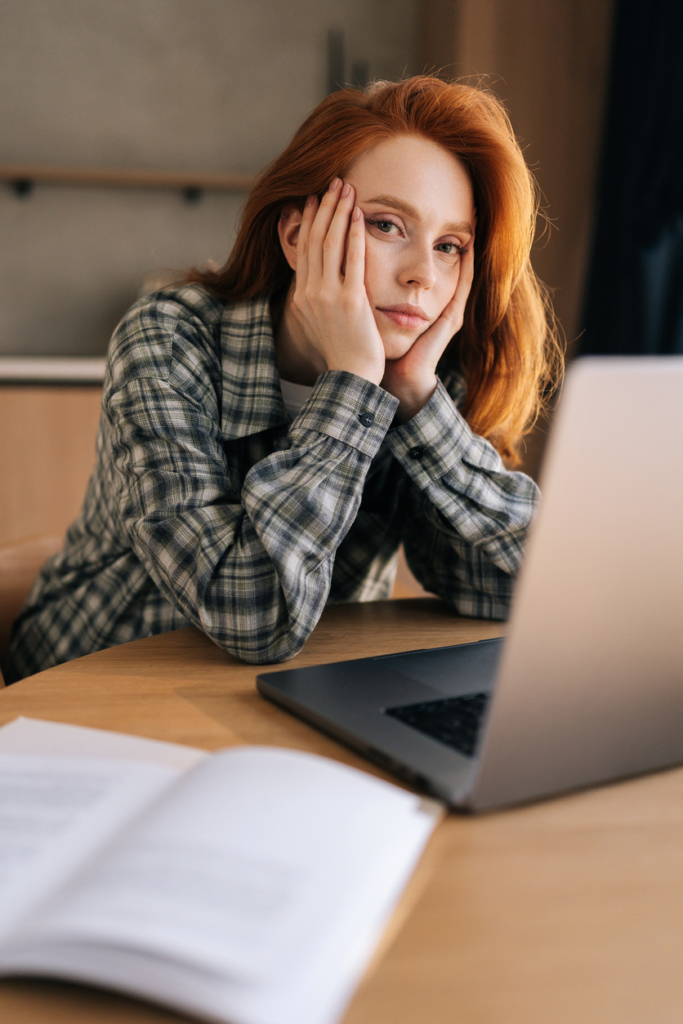 Fiatal, vörös hajú lány könyököl a laptop mellett