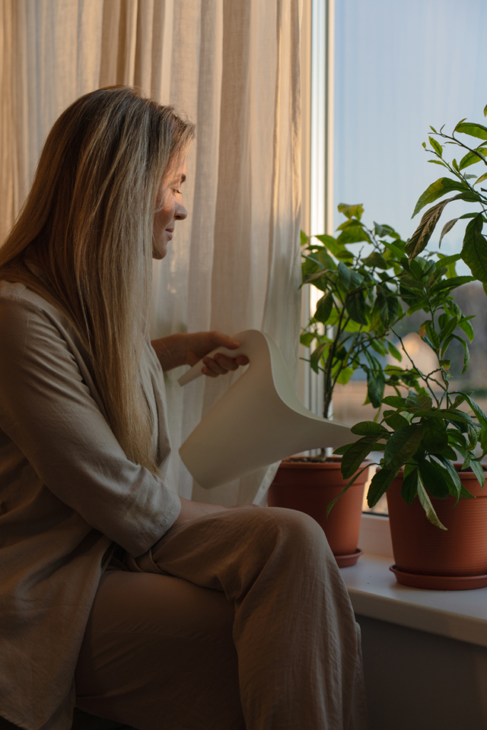 Femme arrosant des plantes d’intérieur placées sur le rebord de la fenêtre