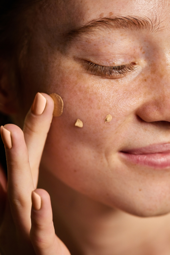 Nő alapozó pöttyöket tesz az arcára