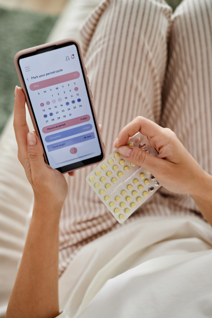 Nő digitális naptárban követi a ciklusát, másik kezében fogamzásgátló tablettát tart