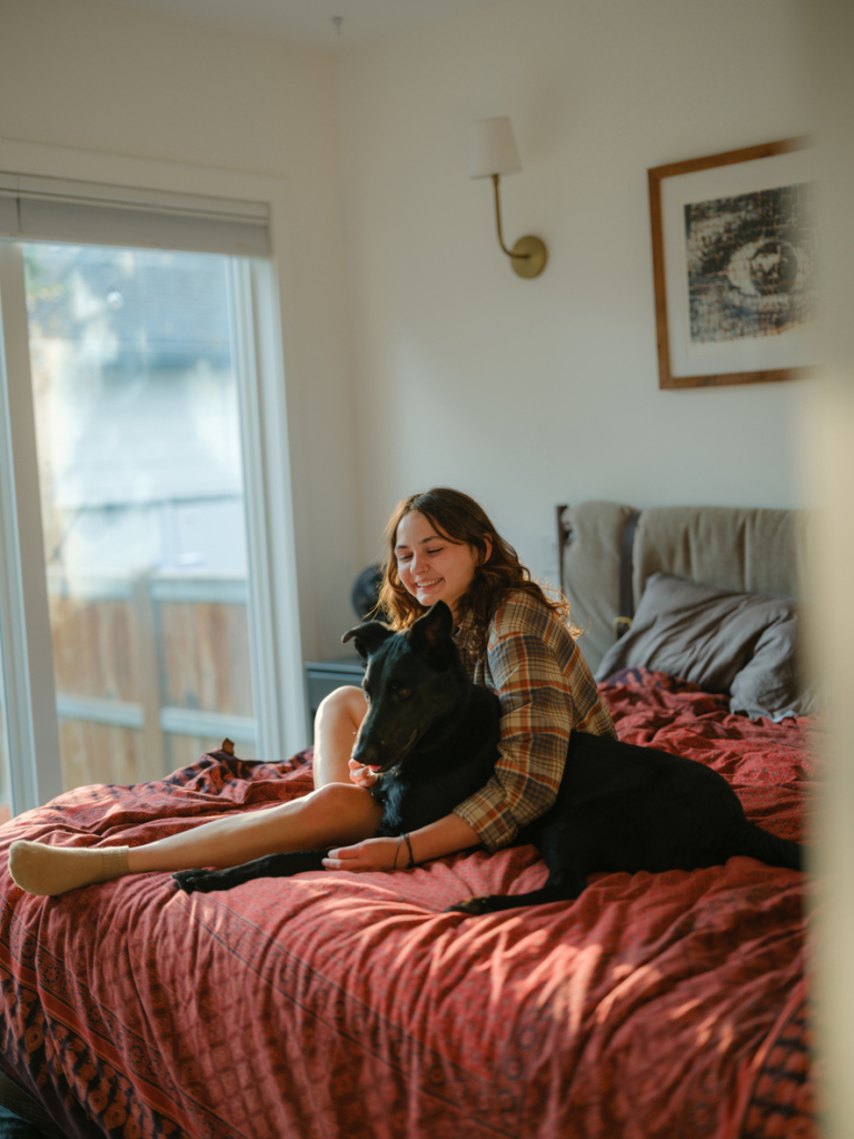 Nő a kutyájával ül az ágyon