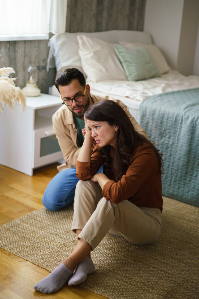 Stresszes nő ül a földön és a párja próbálja vígasztalni