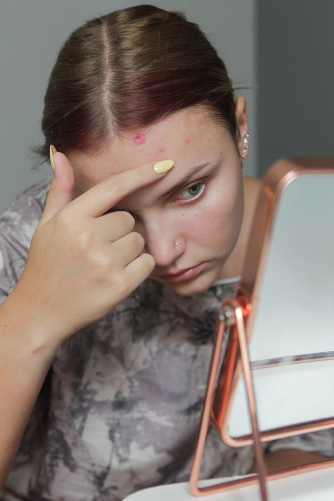 Lány egy kis tükörben nézi a pattanásait