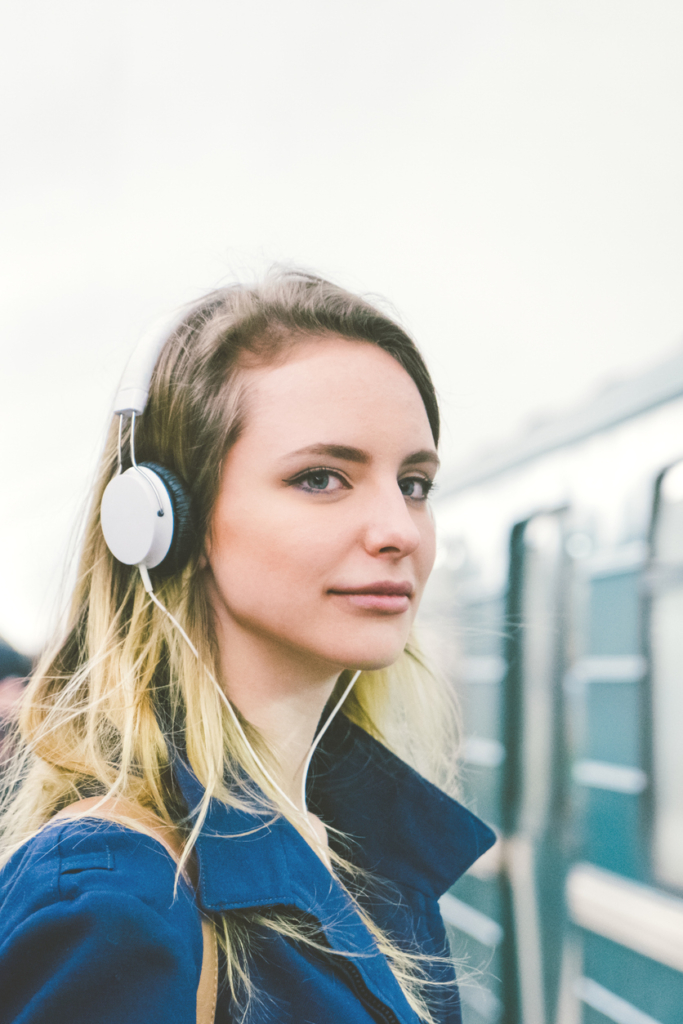 Nő fejhallgatón zenét hallgat, amíg várja a metrót