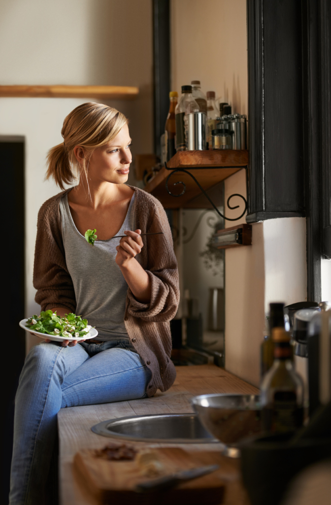 Frau sitzt auf Küchenarbeitsplatte und isst Salat