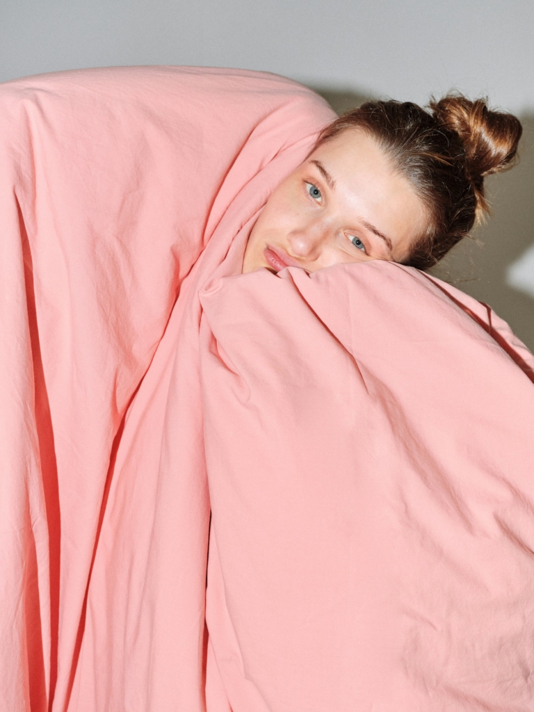 Nő egy nagy rózsaszín takaró alól kukucskál ki