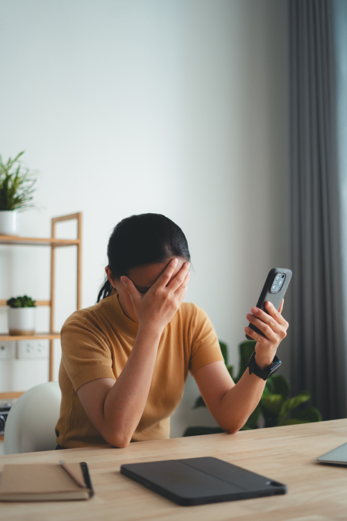 Nő a telefonját nézi, de közben az arcát a tenyerébe temeti