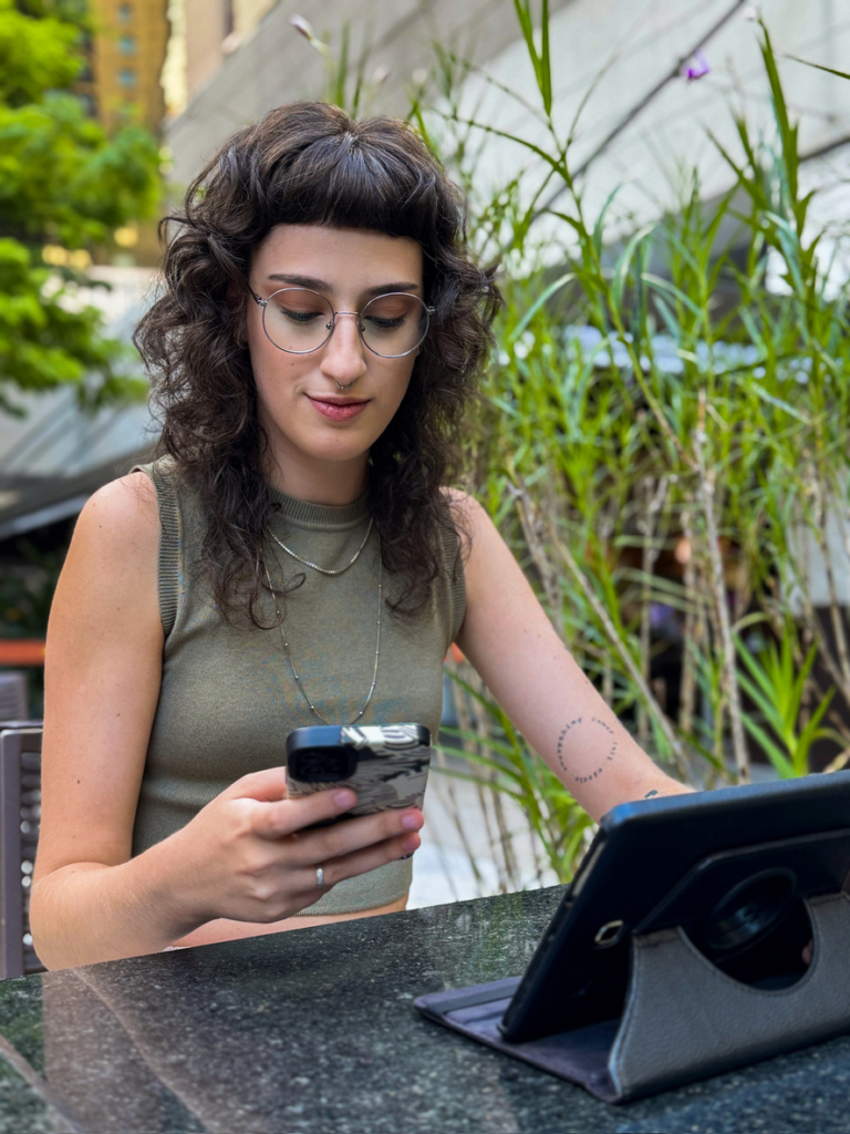 Fiatal nő egy kávézó teraszán dolgozik a tabletjén