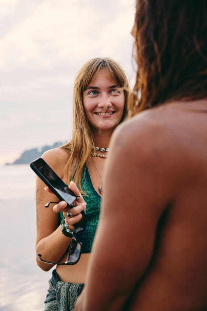 Nő átadja a mobilját egy férfinak a vízparton