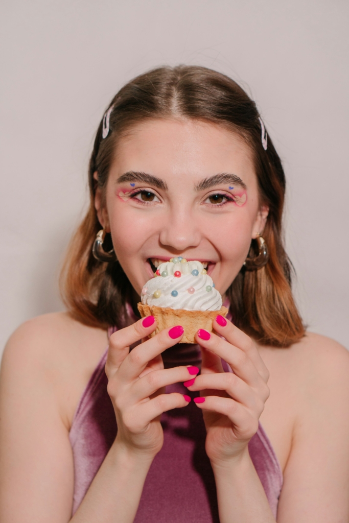 Fiatal, mosolygós lány egy cukorkagyöngyös muffinnal a kezében