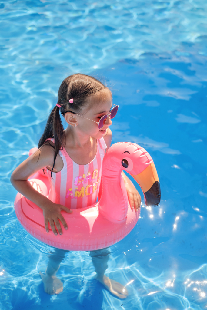 Kislány pink fürdőruhában egy rózsaszín flamingó úszógumival