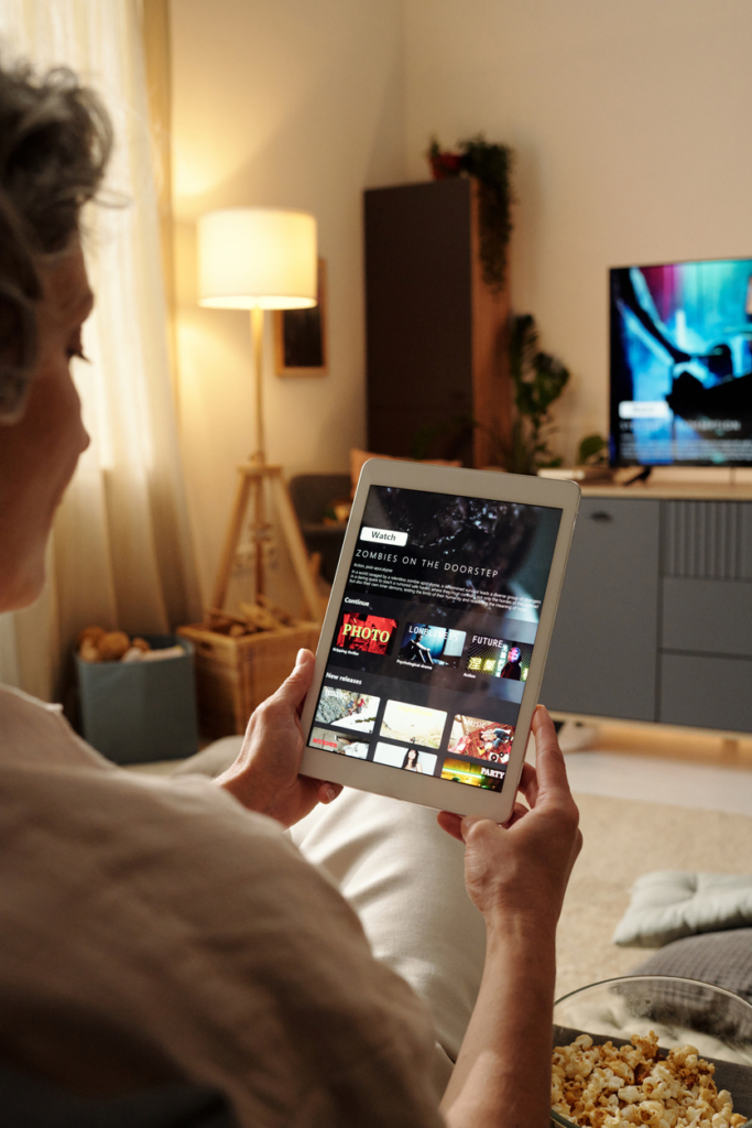Idősebb nő kezében tablet, amin a Netflixet nézi