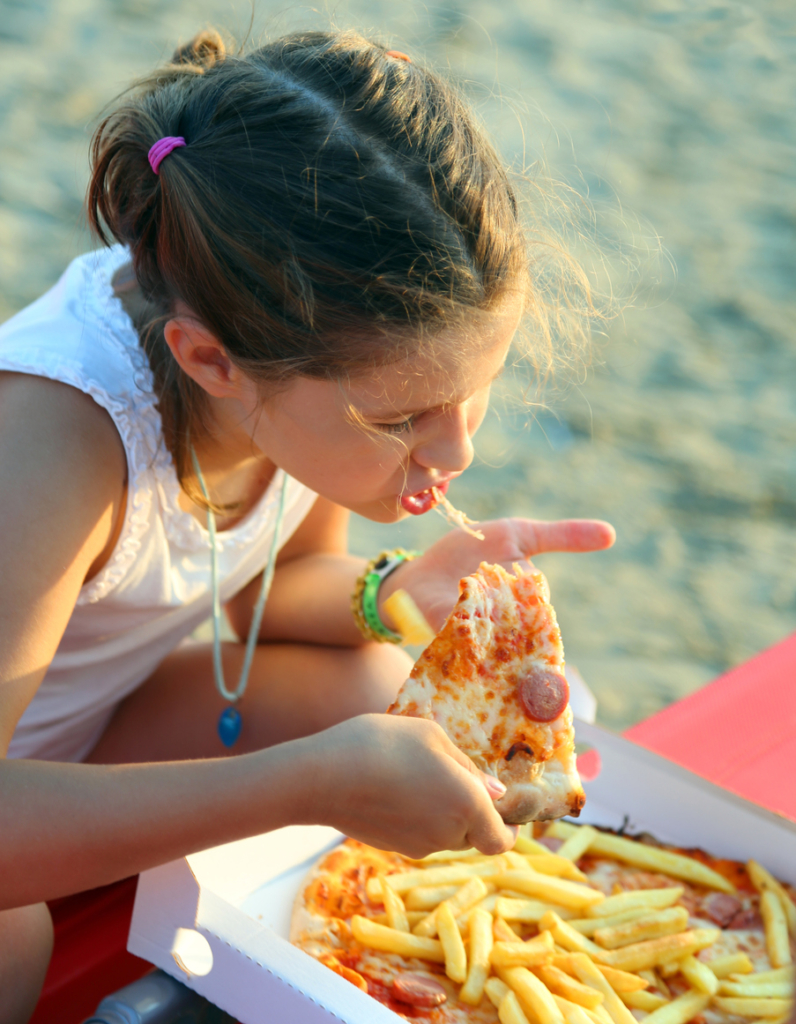 Kislány pizzát és sültkrumplit eszik a strandon