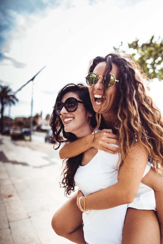 Due donne ridono a crepapelle, una sulle spalle dell'altra