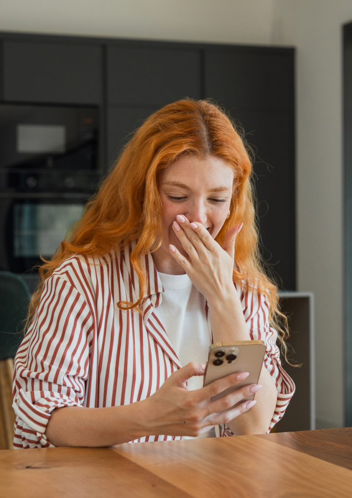 Nő a szája elé teszi a kezét, miközben a mobilján olvas
