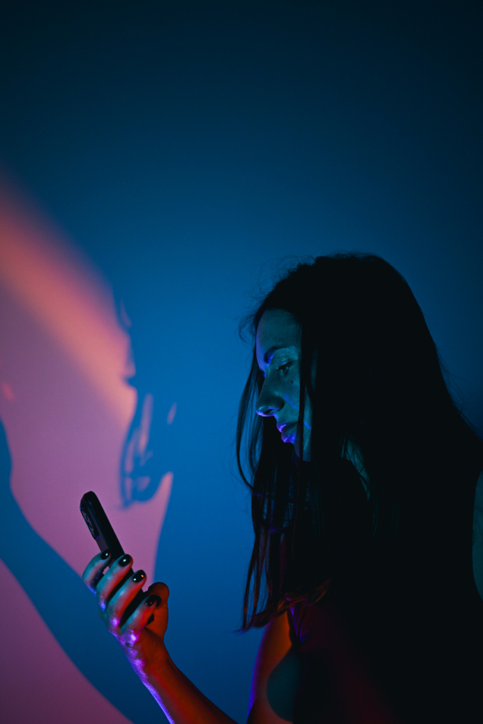 Nő neon fényekkel megvilágítva, ahogy a telefonját nézi