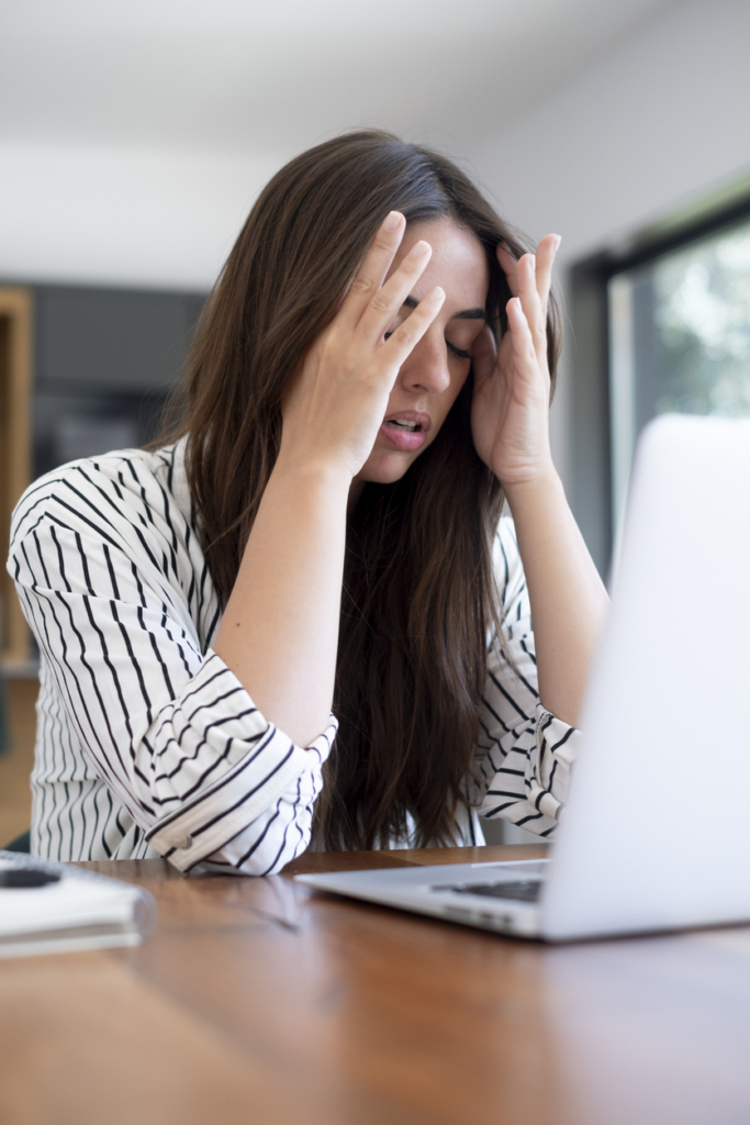 Túlterhelt nő a laptopjánál ül és fogja a fejét