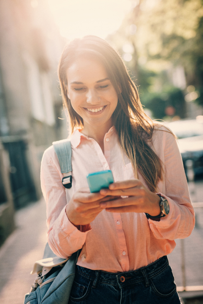 Nő sms-ezik a napsütötte városi utcán