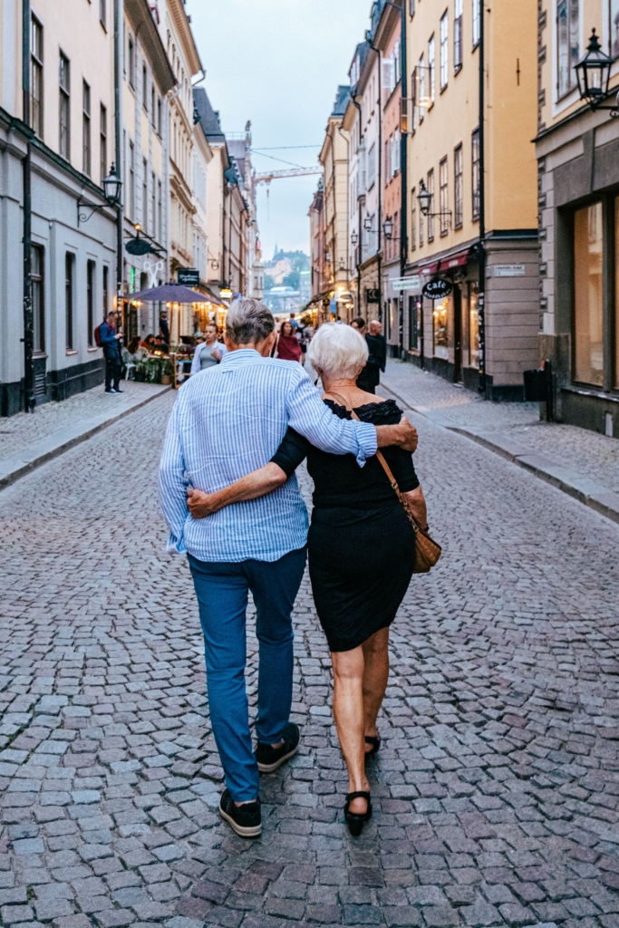 Középkorú pár háttal sétál a városi utcán, egymásba karolva