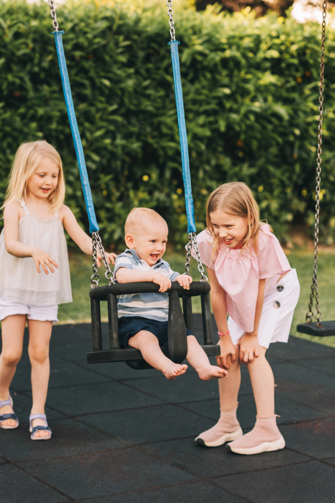 Két kislány a babahintában lök egy kisfiút