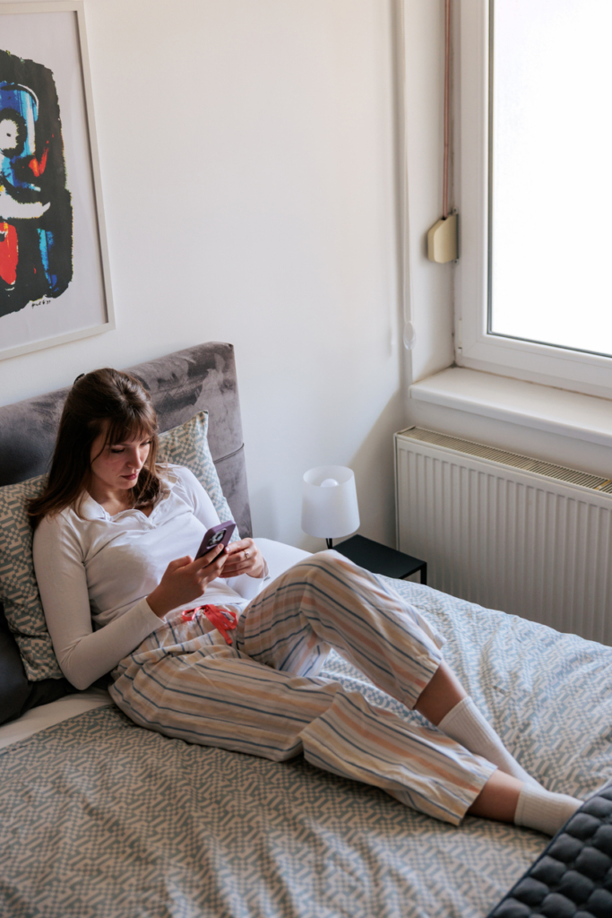 Nő az ágyban, pizsamában a telefonját nézi