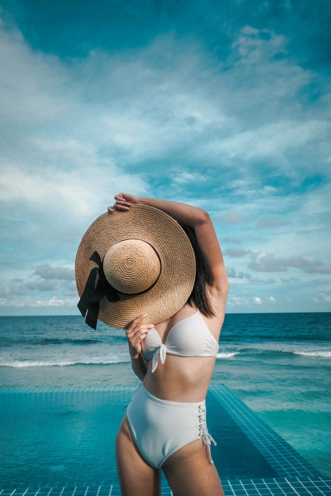 Bikinis nő az arcát takarja a szalmakalapjával