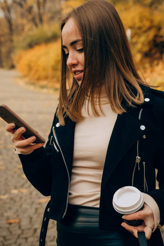 Nő a kezében a telefonjával és egy kávéval