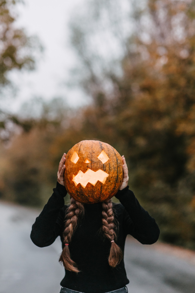 Nő egy kifaragott Halloween-i tököt tart az arca elé az úton