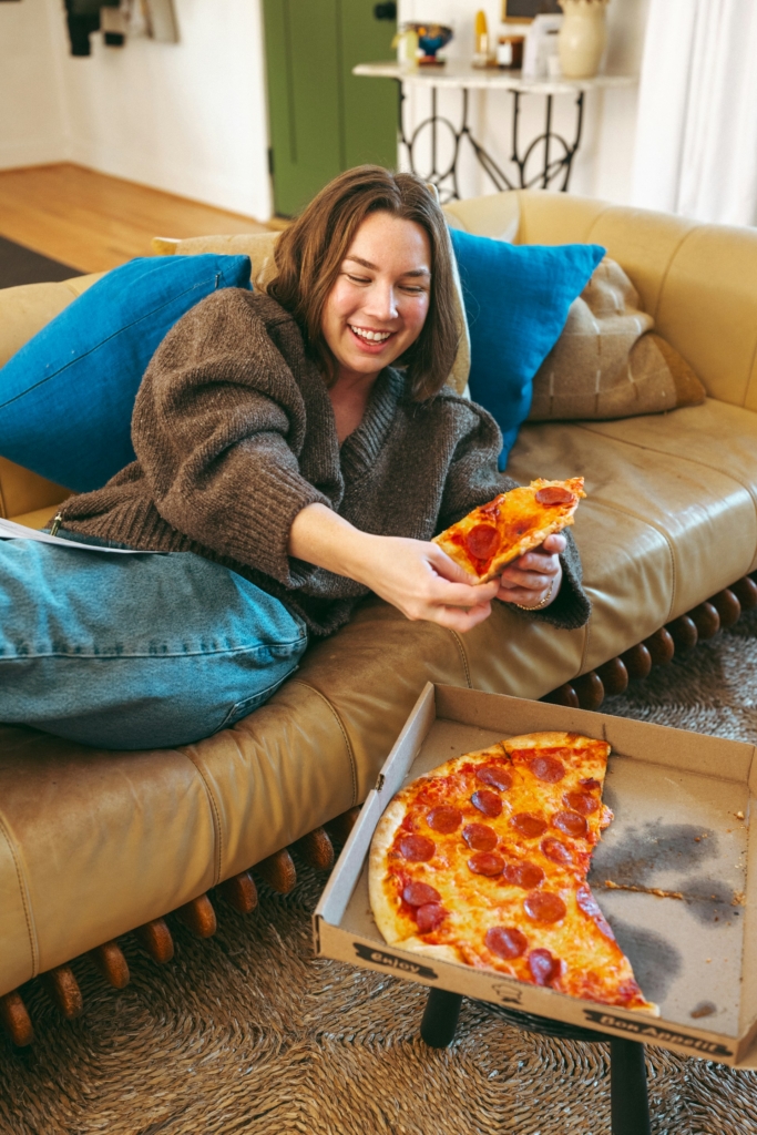 Nő egy nagy szalámis pizzát eszik a kanapén fekve
