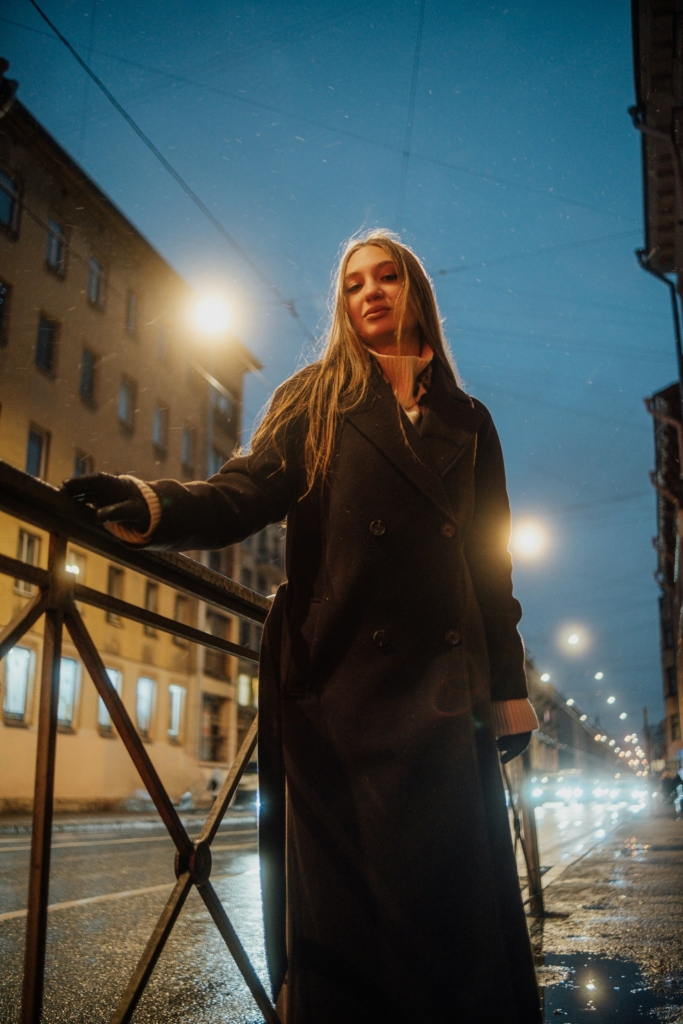 Nő áll egy korlátnál az esti városban